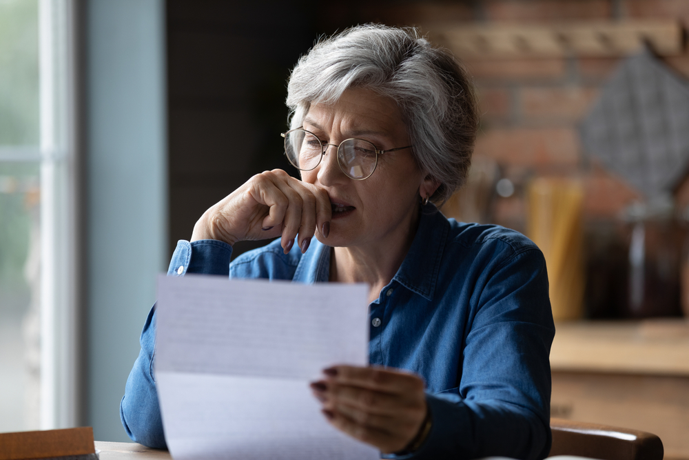 Seated old woman biting nail while holding eviction letter with other hand